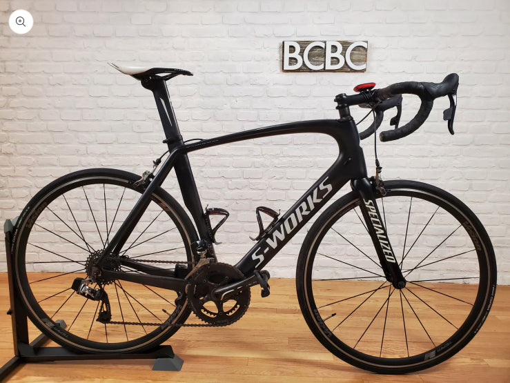 A collection of pre-owned carbon fiber road and gravel bikes from top brands like Trek, Specialized, and Cervelo, displayed in a professional bike shop setting.